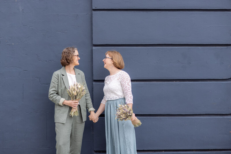 Mature and relaxed brides holding hands in front of navy  building