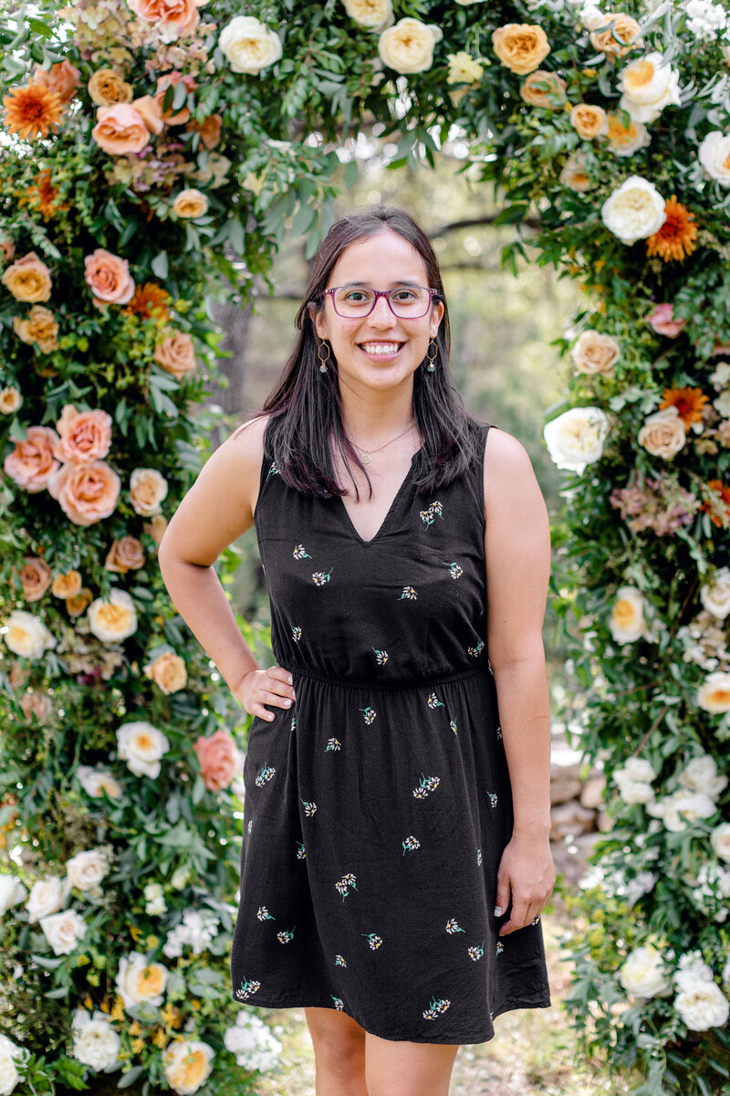 Austin Texas wedding planner Veronica poses in front of an orange floral arch