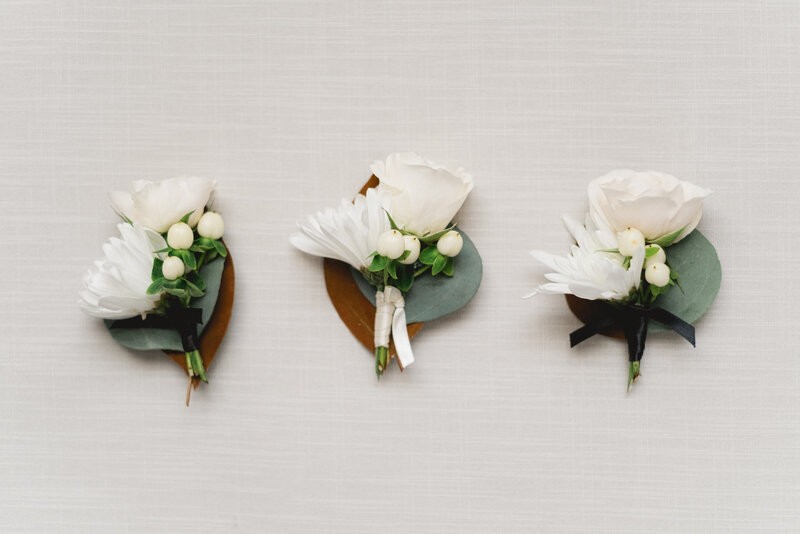 three wedding day boutonnieres with white roses set in a row