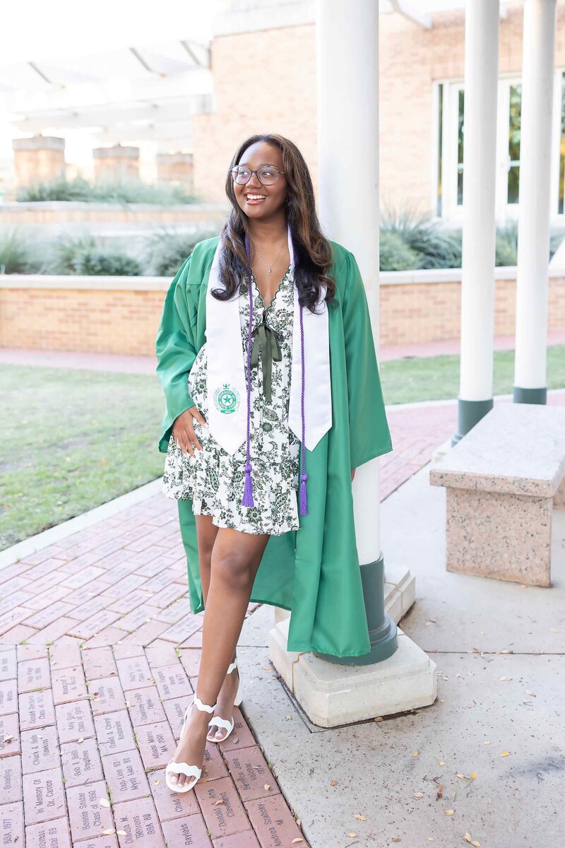 DFW senior photo session featuring a joyful graduate woman in a green cap and gown, captured for the Senior Photography Portfolio by Sophie K. Hunter.