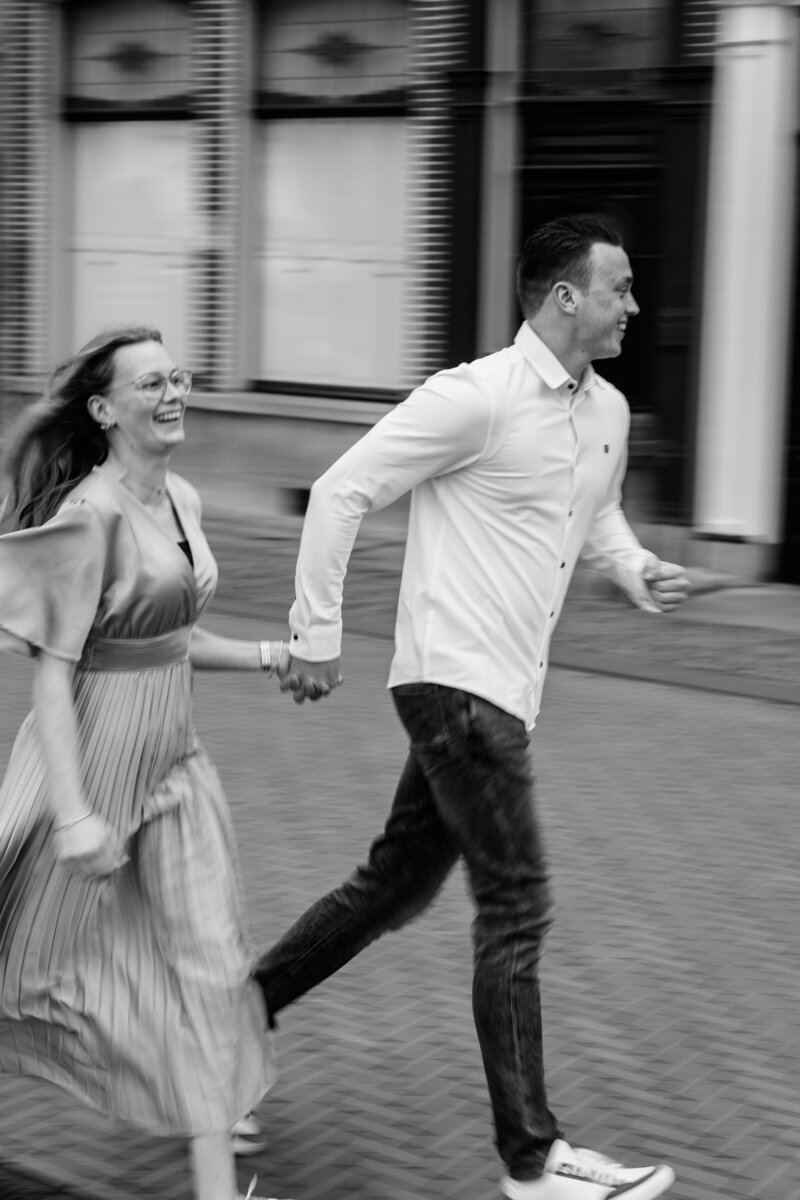 Een stel rent hand in hand door de stad in een zwart-wit loveshoot, vastgelegd door Monica Stout Fotografie voor een spontane en speelse sfeer.