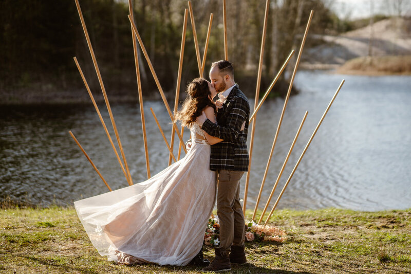 Troujurk en trouwpak, bruidspaar kus bij de ceremonie aan het water
