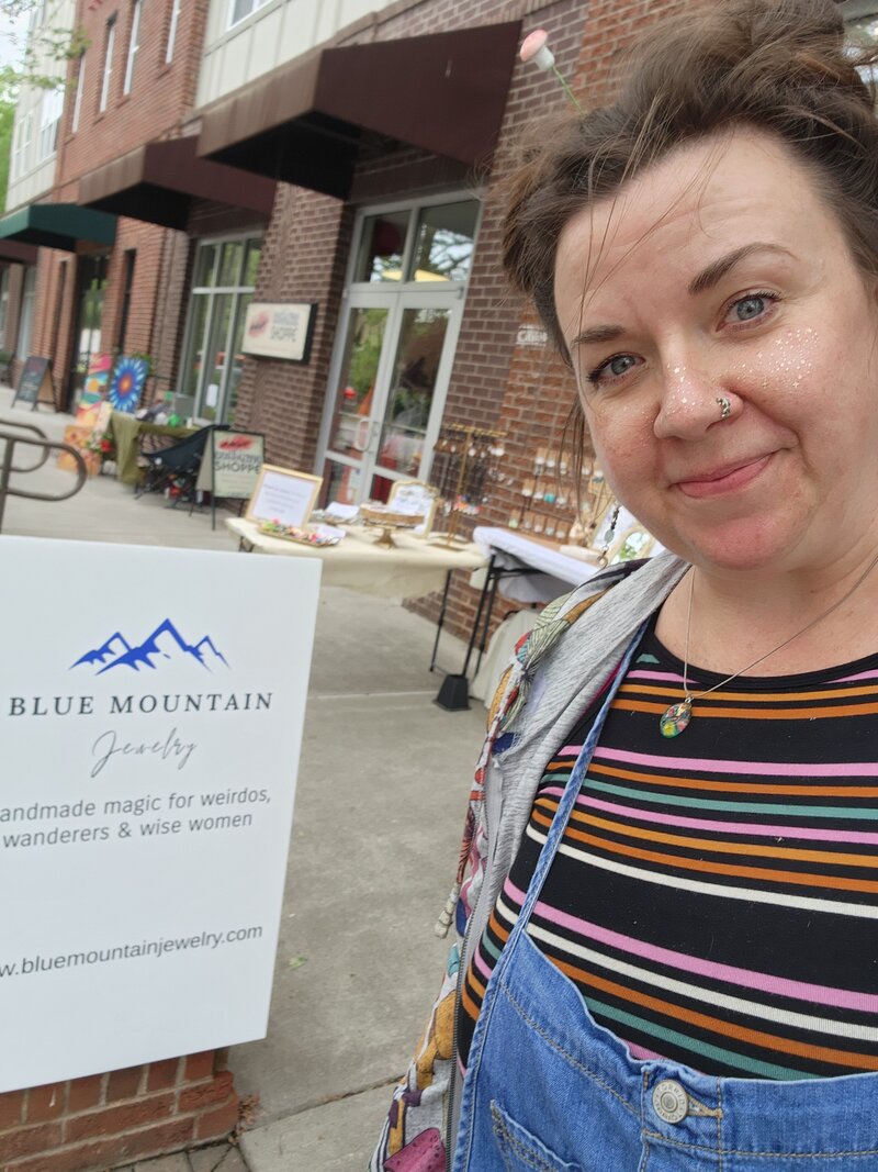 The Founder of Blue Mountain Jewelry smiling in front of her logo 