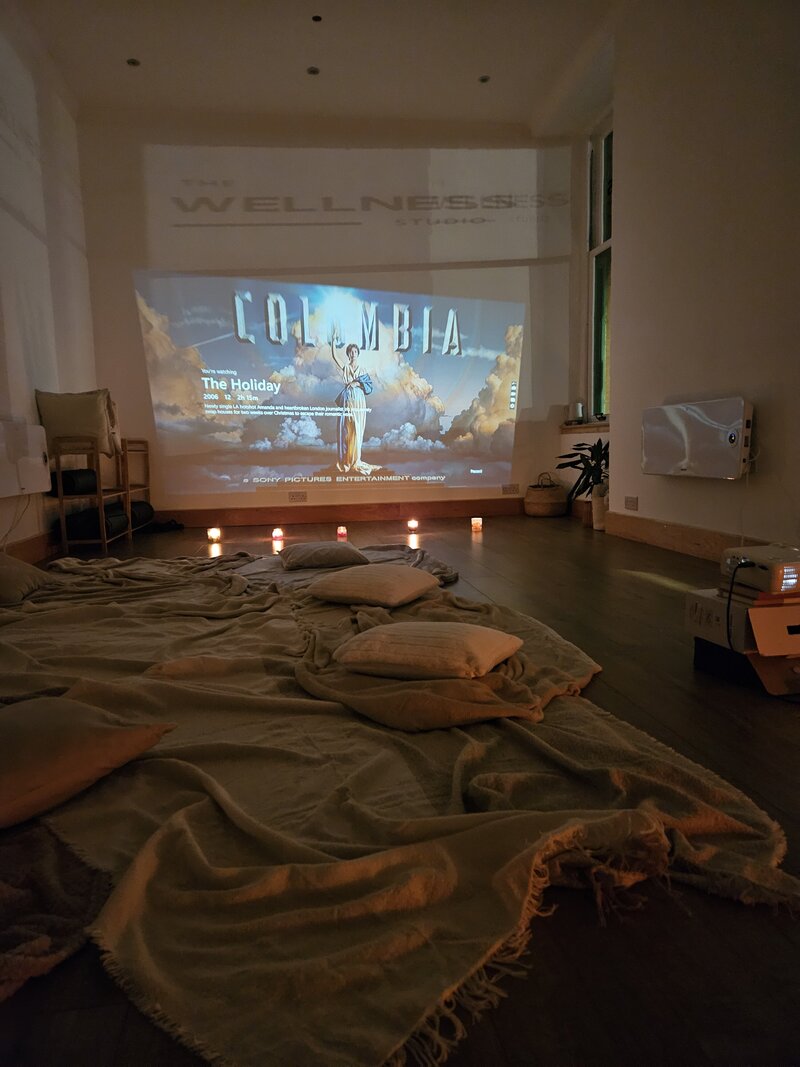 A cosy night in the studio with a movie on the projector, sitting on the floor on blankets and cushions with candles around.