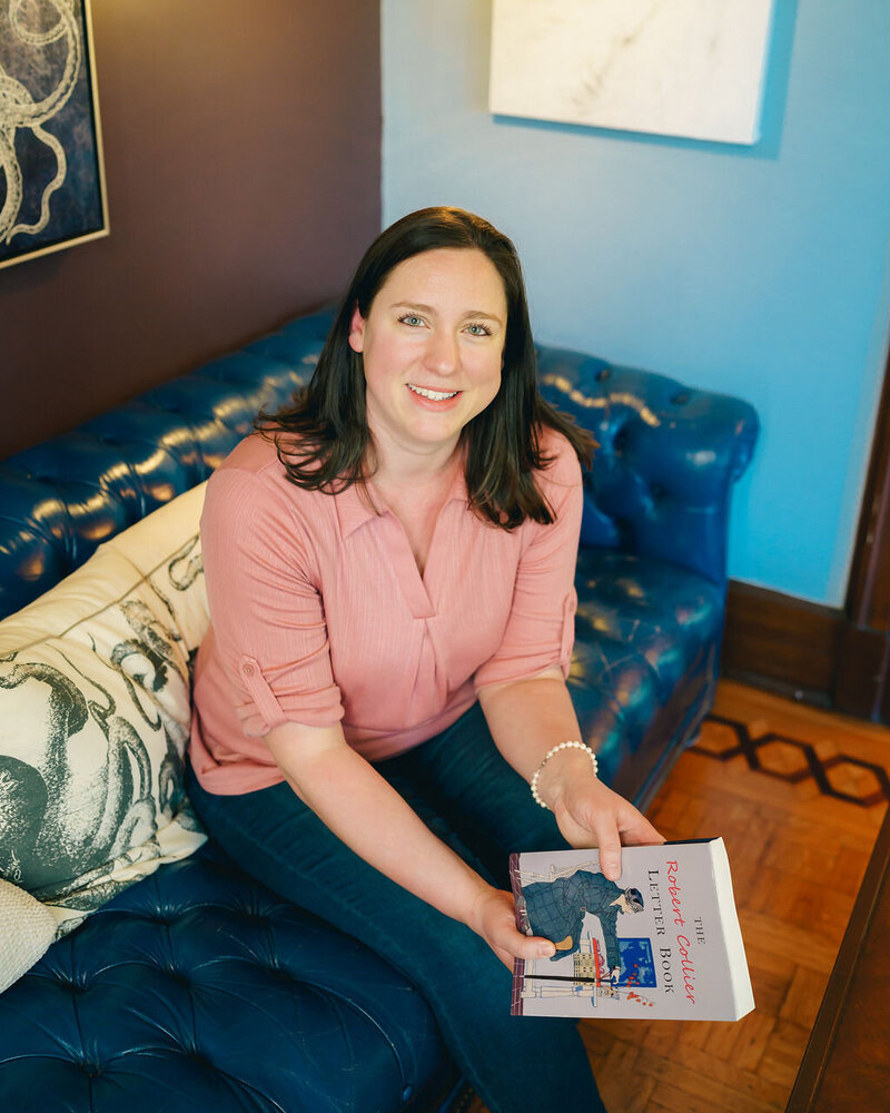 Kat Jackson sitting on a vibrant blue couch holding a book to demonstrate brand messaging services.