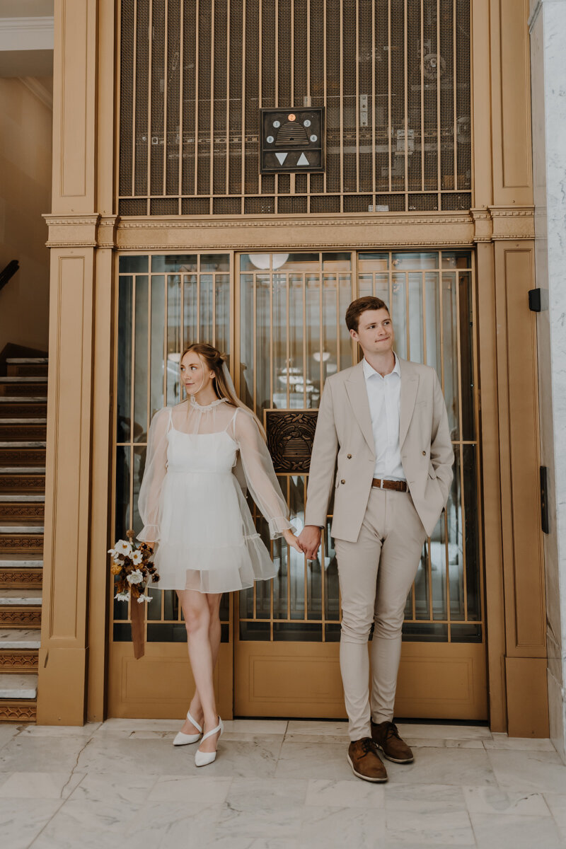 bride and groom holding hands while standing in fron of large glass window