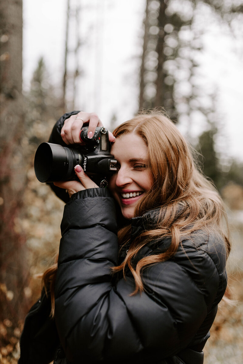 The photographer is holding up her camera to take a photo and is smiling before she takes it.