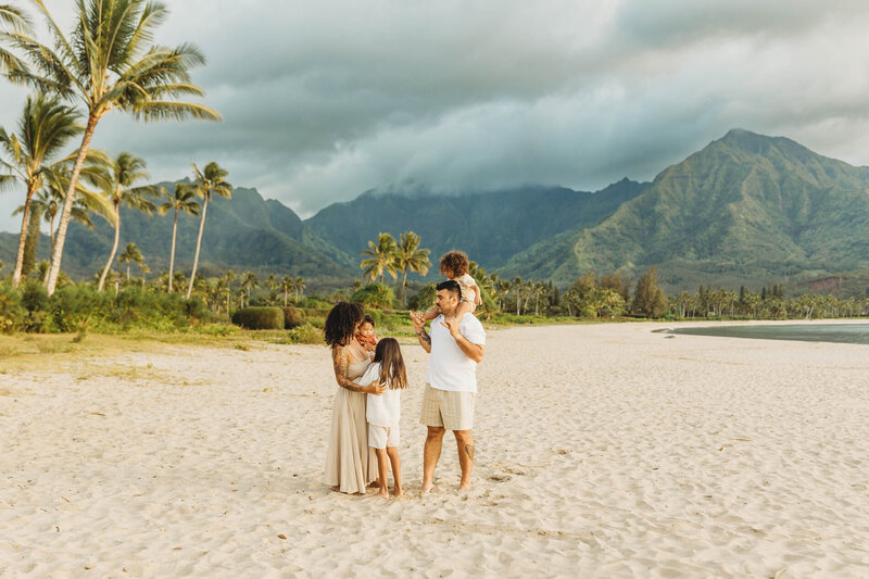 Family playing together on the beach with lush mountains and palm trees in the background — joyful Kauai family session by Leslie Carbajal Photography