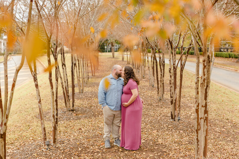 Pregnant mom cradles belly as she kisses husband during maternity session in Hoschton