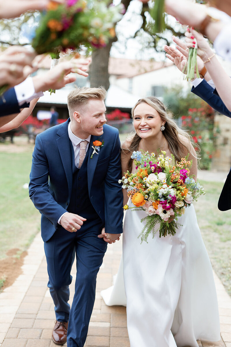 Bride and groom going under a spirit tunnel with their wedding party with flower bouquets