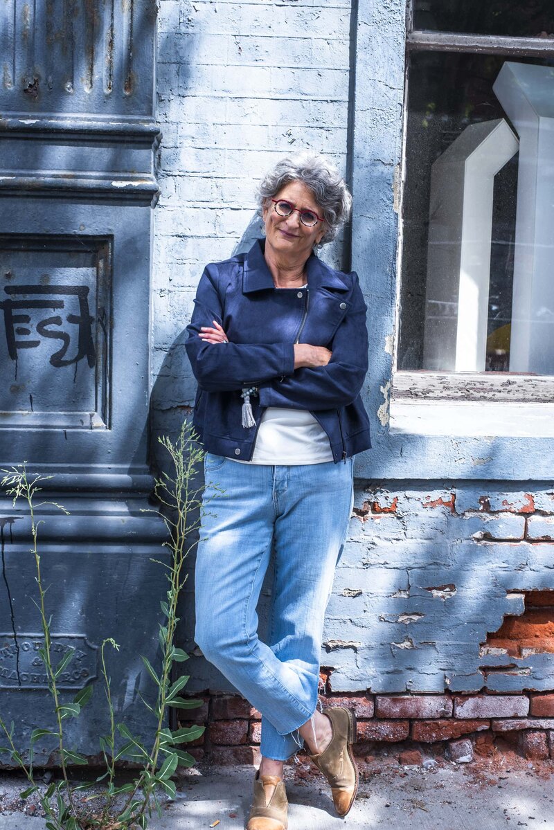 Amy Posner leaning against a blue wall outdoors