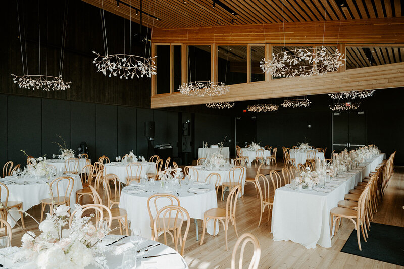 Reception tables with lucite vases of white and neutral-toned florals, pale Bentwood chairs, and candlelight at Jenay and Daniel’s modern romantic wedding, by Summer Robbins Flowers in Central Oregon
