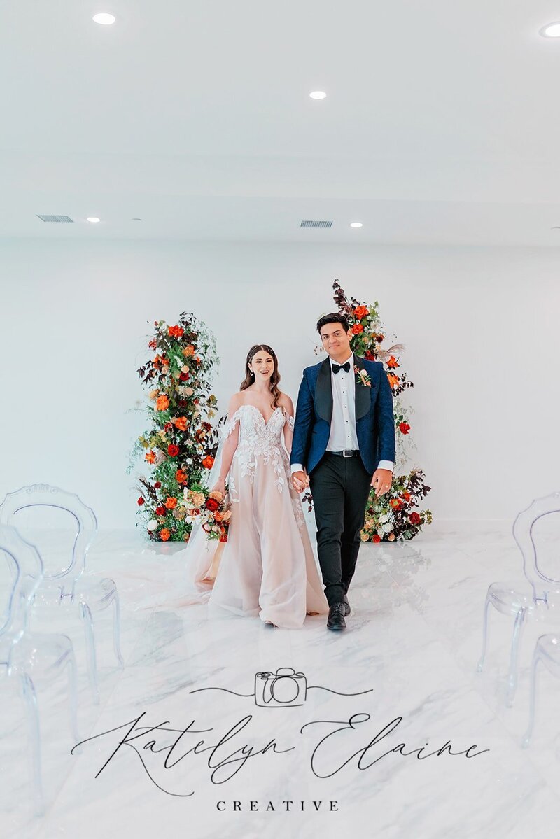 Acrylic Queen Chairs border the image in an all white room with a fashionable married couple with  an archway behind them.