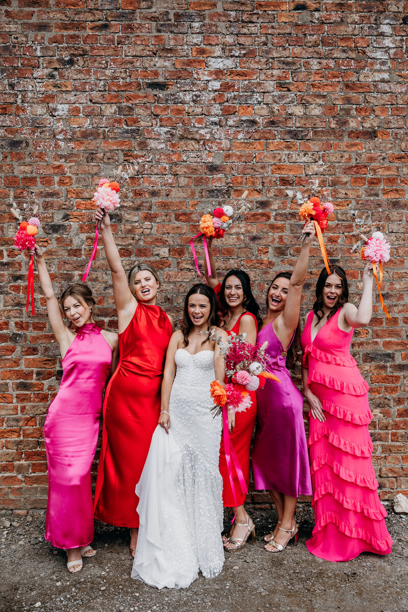 Bride and her bridesmaids wearing pink and red celebrating with flowers