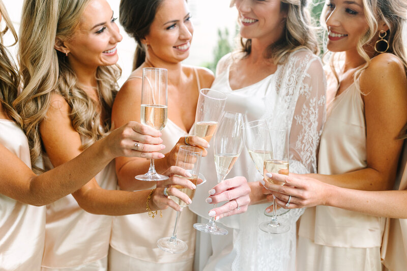 close-up image of a bride and her bridesmaids smiling and cheersing their champagne.