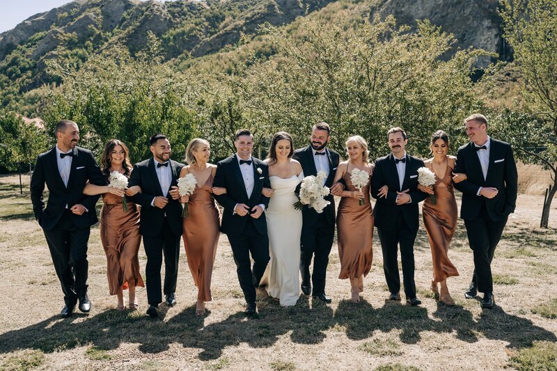 a bridal party in black and white and rust colour satin dresses in front of mountains in queenstown