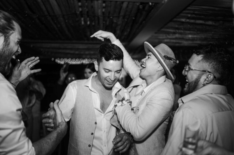 a black and white photo of guests dancing at a beach wedding.