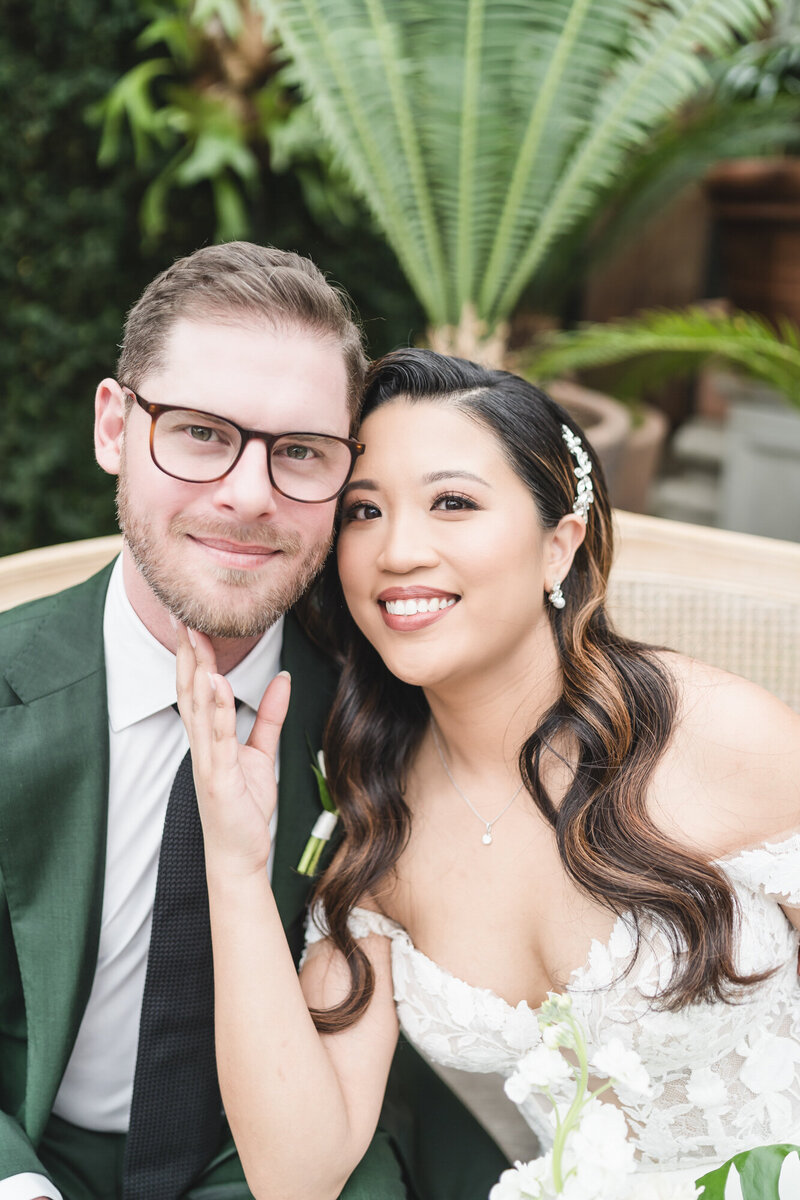 Bride gently holds groom’s face as they sit close, smiling with love and trust on their wedding day at Planterra Conservatory