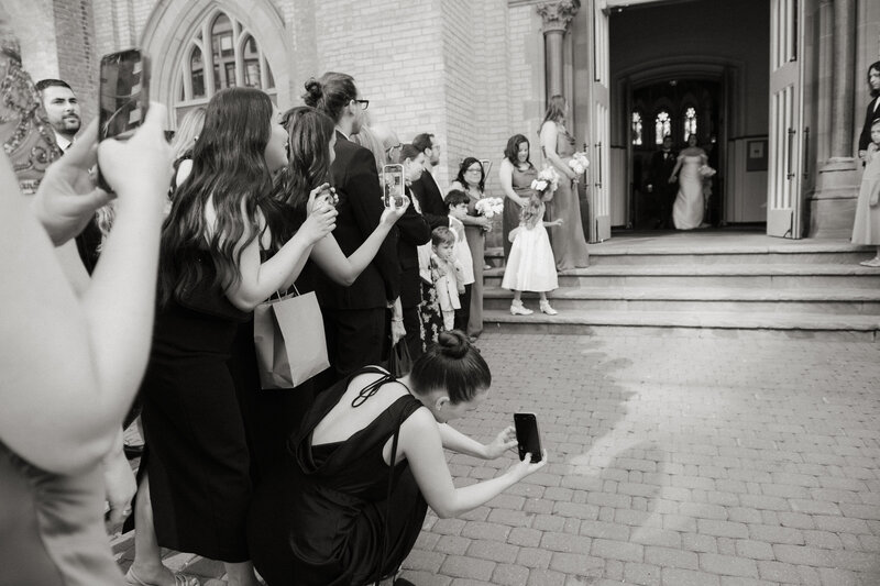 wedding guests taking photos of bride and groom as they gleefully exit a downtown toronto church after their wedding ceremony