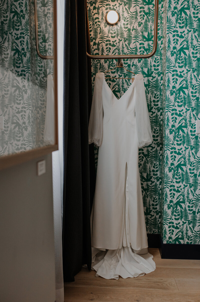 White wedding dress hanging in front of wall with green wall paper