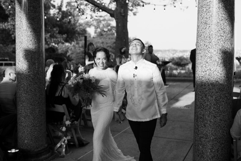 Black and white image of bride and groom walking down the aisle smiling