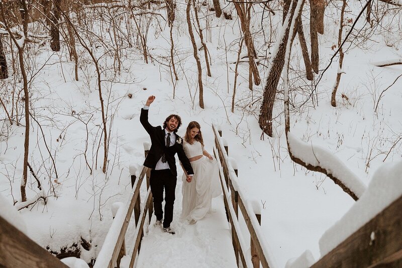 bride and groom walking across a bridge surrounded by snow