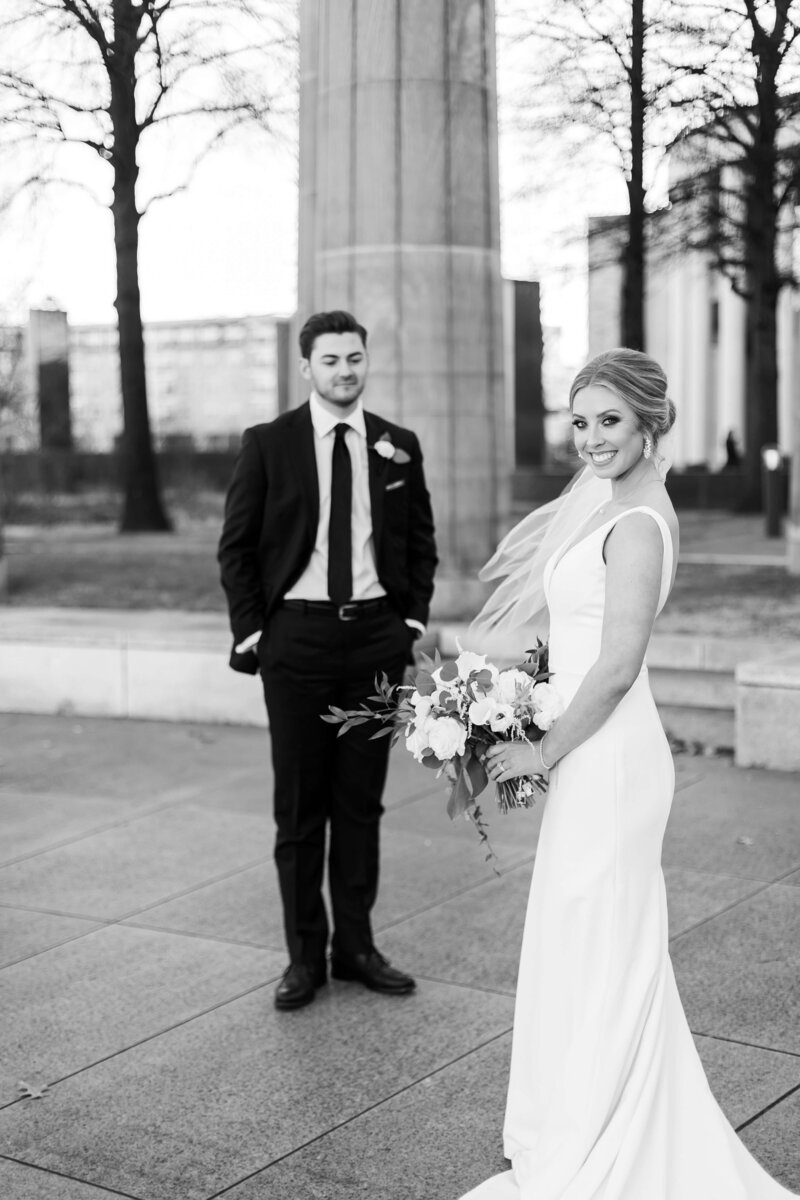 Groom looking at bride as she holds bouquet and looking at camera