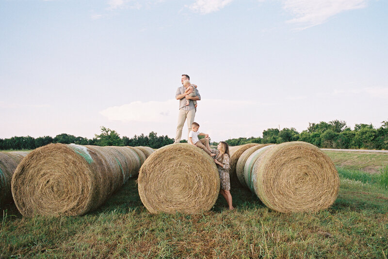 Family of four playing on hay bales in a grassy field