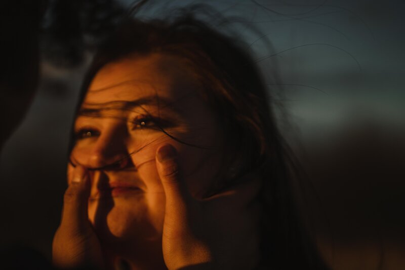 A man holds the face of his girlfriend in the sunset with a farm in the background.