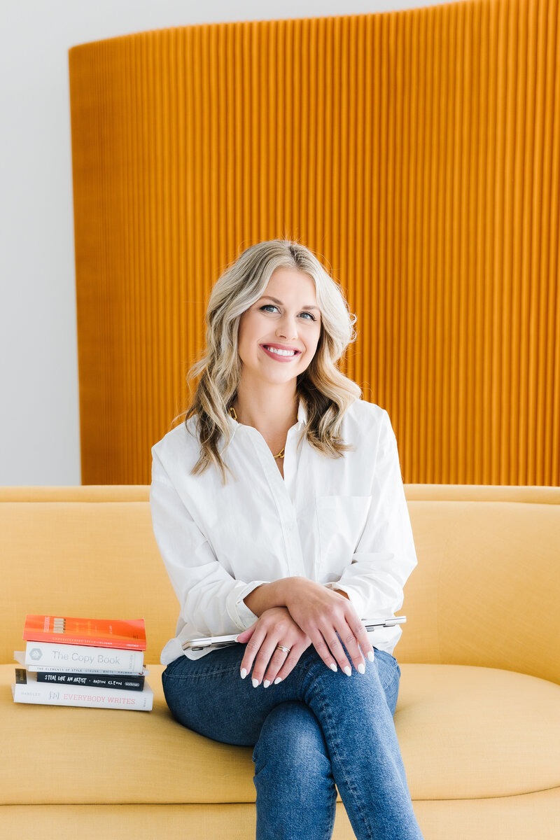 Sarah Klongerbo standing in front of magazine pages hanging on clothespins and wearing black jeans and a white top with letters all over it