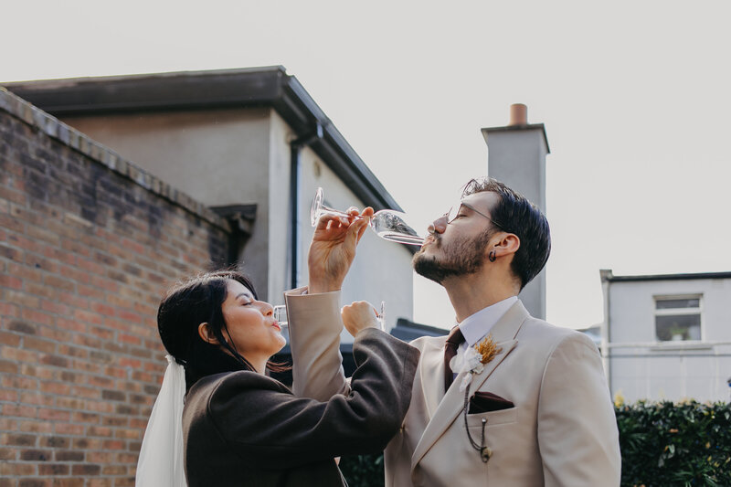 Newlyweds toasting with champagne, arms intertwined in a playful and romantic gesture in Dublin General Register Office.