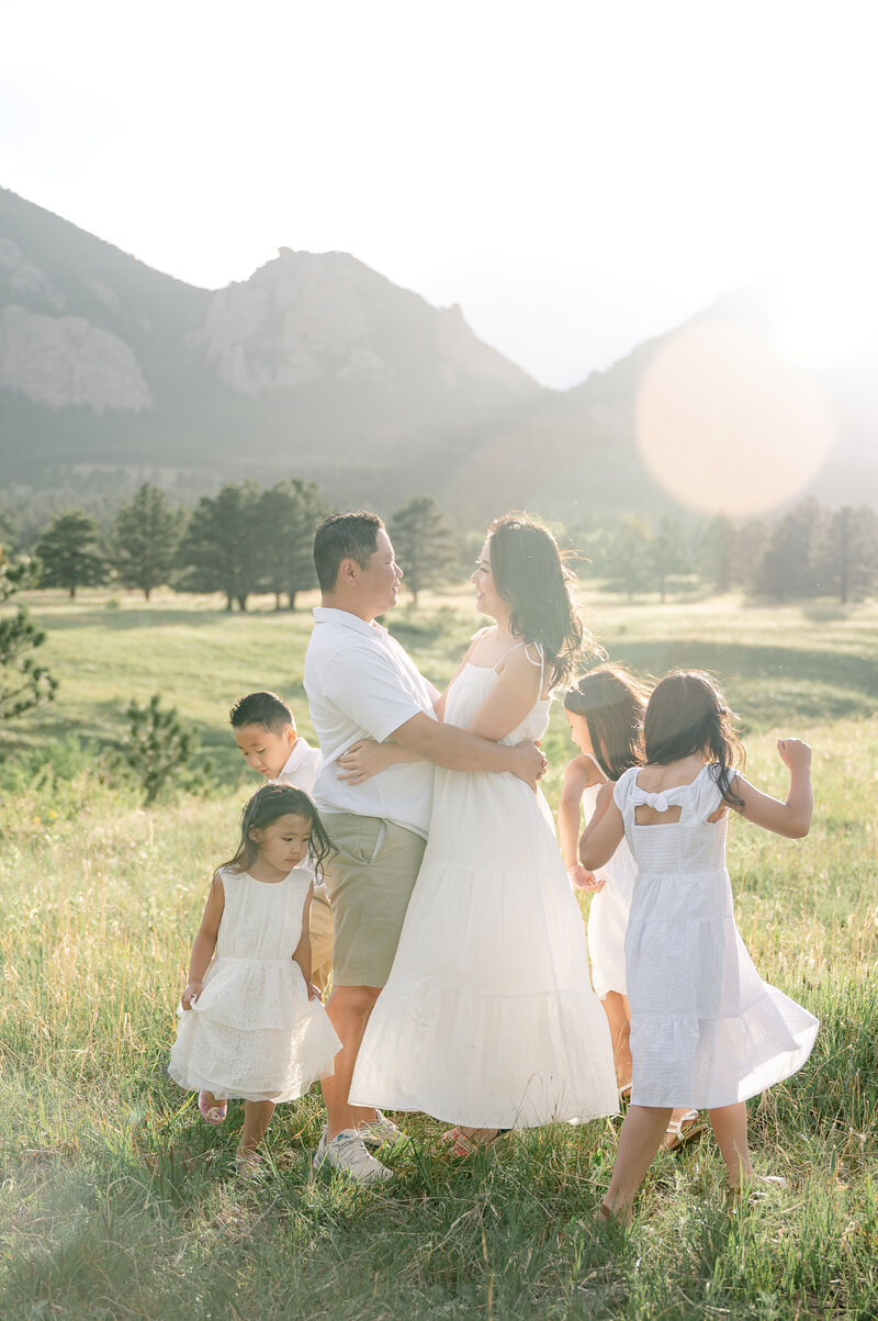 Kids dancing around mom and dad during a family portrait session with mountains in the background in Colorado