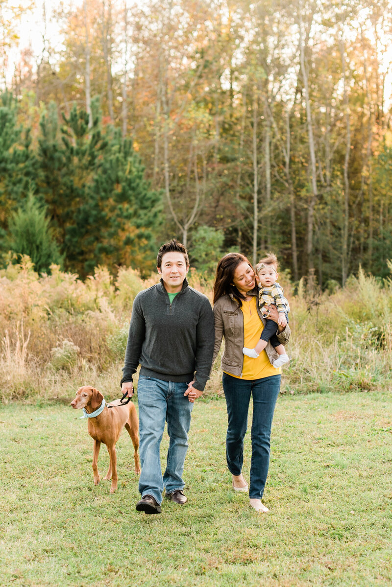Family walking and smiling as they play for a moment with their dog during their Raleigh family session. Photographed by Raleigh family photographers A.J. Dunlap Photography.