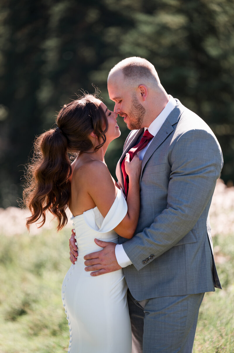 bride pulls groom in for a kiss standing in a field at Whitemud Park in Edmonton