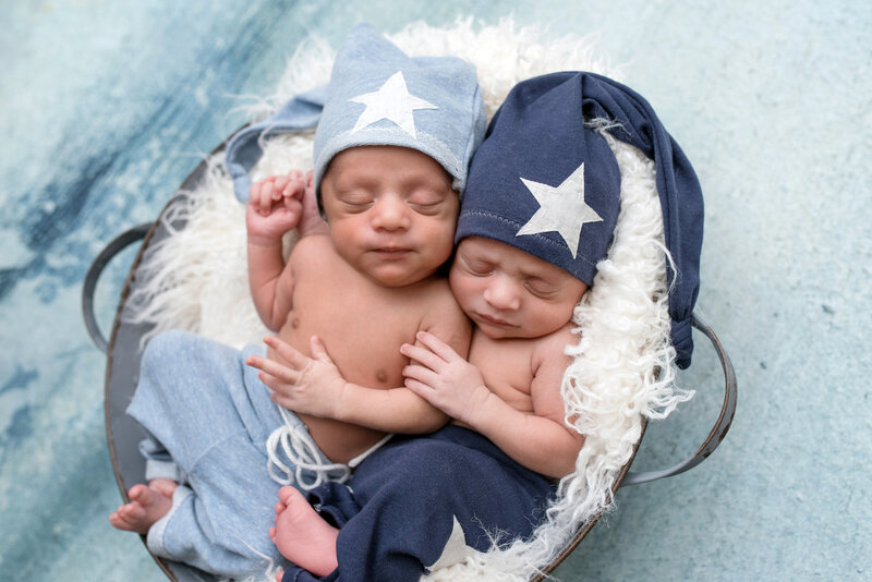 Newborn twin baby boys lying in bowl during their newborn session.