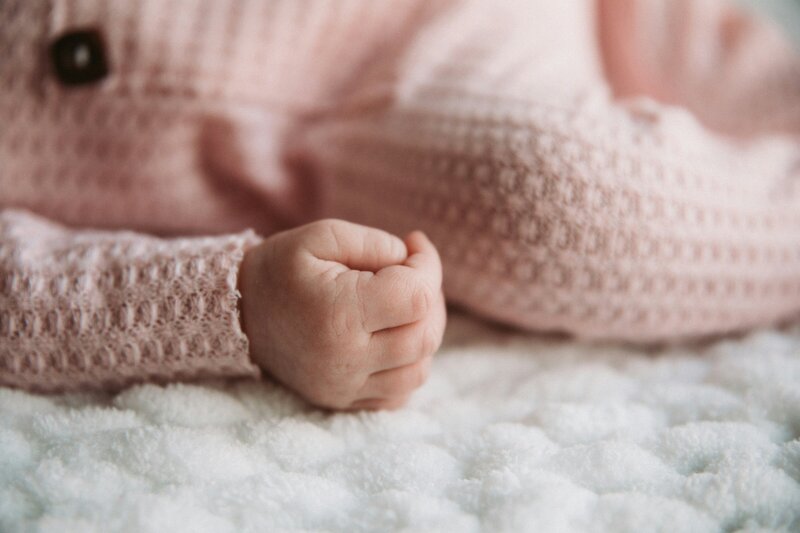 Close up of baby's tiny hand in a soft pink sweater, symbolizing tenderness, new beginnings, and the love adoption makes possible.