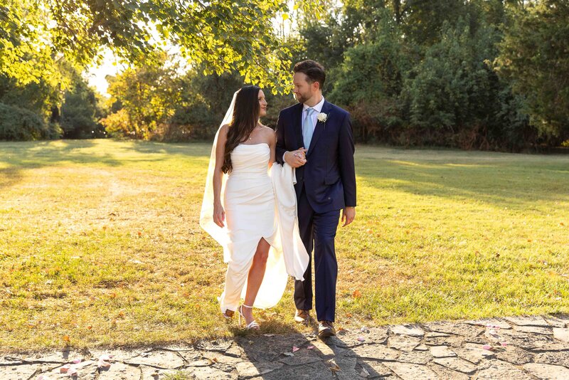 bride and groom walking across green grass while smiling at each other