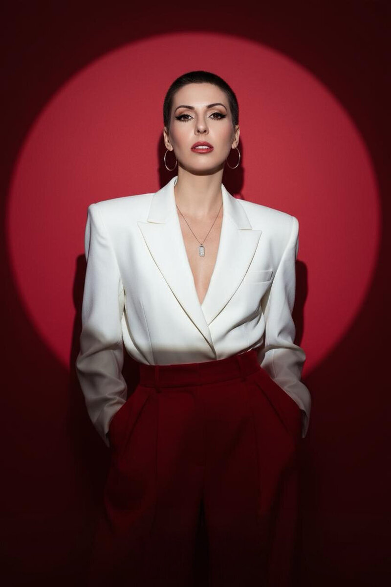 Jasmina Kimova standing confidently in a white blazer and red trousers, framed by a red spotlight, symbolizing identity reinvention and cinematic presence.
