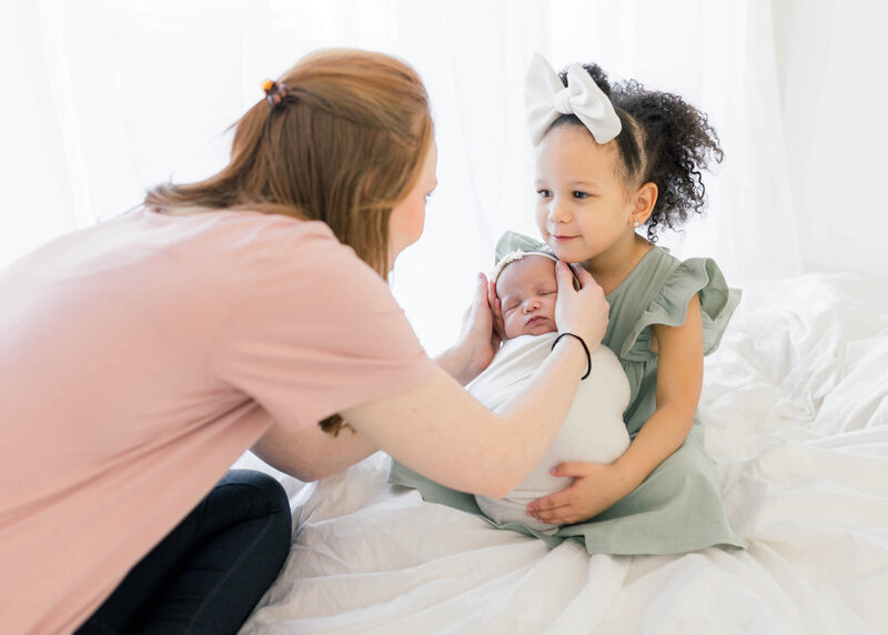 okc photographer posing a newborn with her older sister holding her