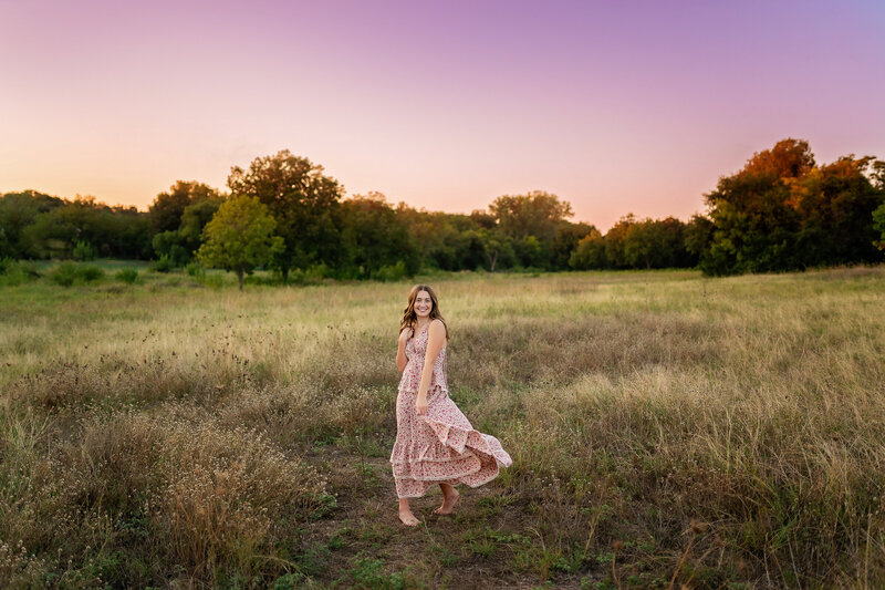 An oklahoma City senior student poses in a field at sunset.