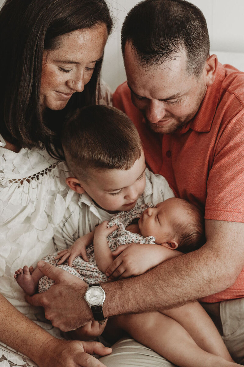 Mom and dad helping young son hold newborn baby.