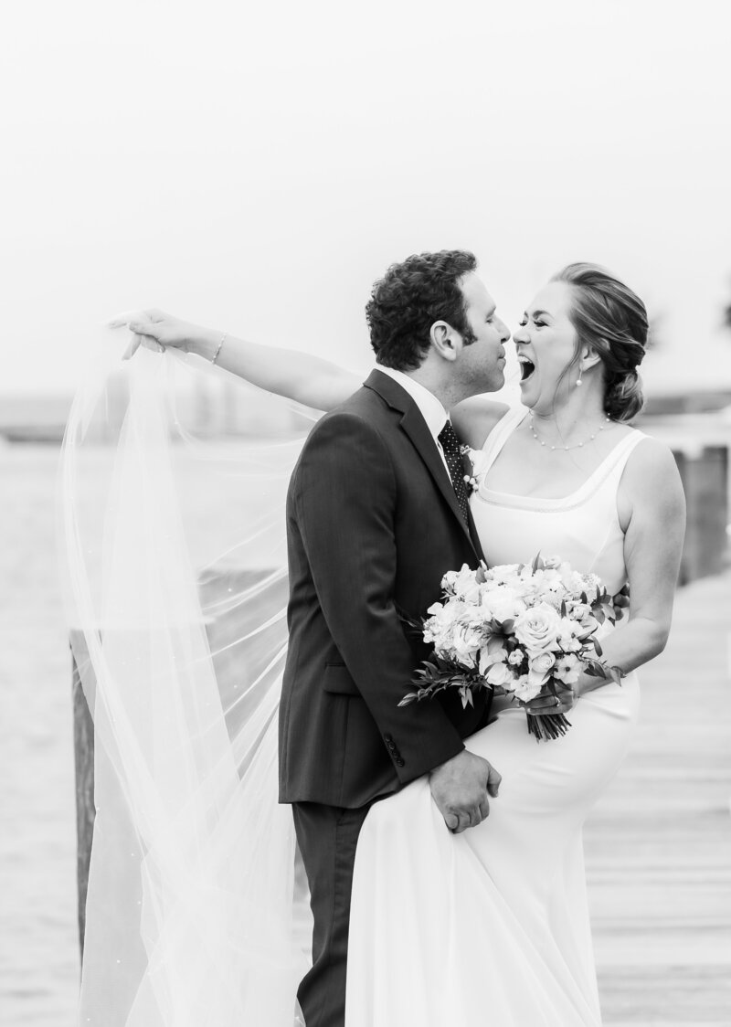 Bride laughs exuberantly at groom on the pier at Annapolis Maritime Museaum, Wedding
