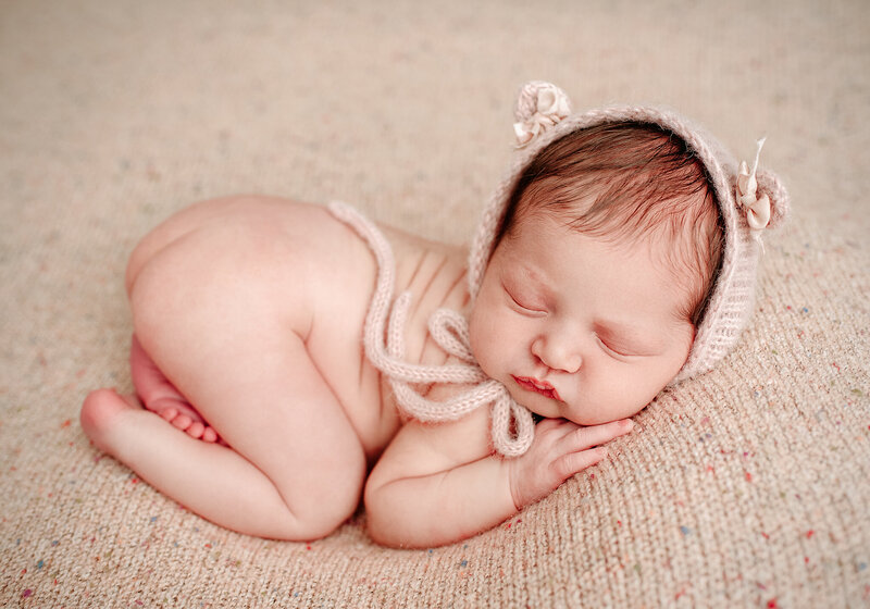 Newborn girl on pink backdrop wearing bear bonnet in Jacksonville, FL.