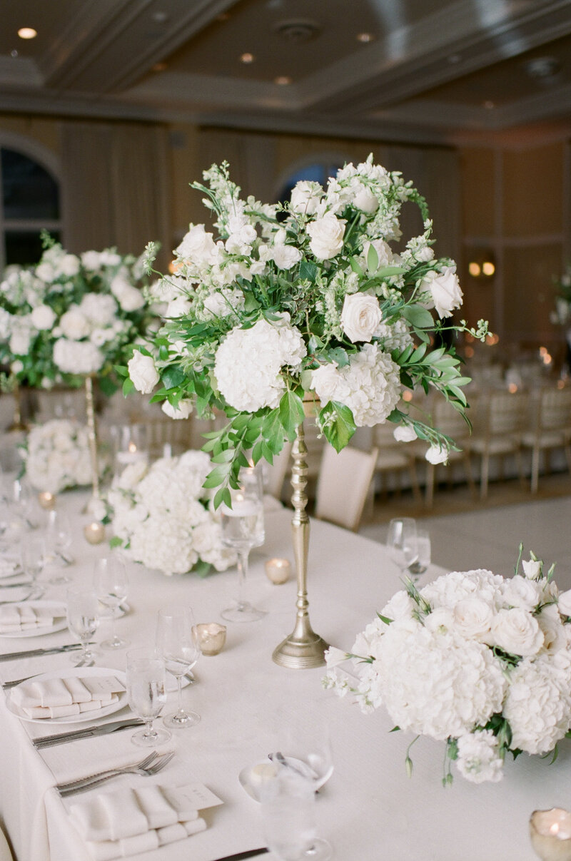 Indoor wedding reception space, with all white decor and flowers in tall, skinny, golden vases.