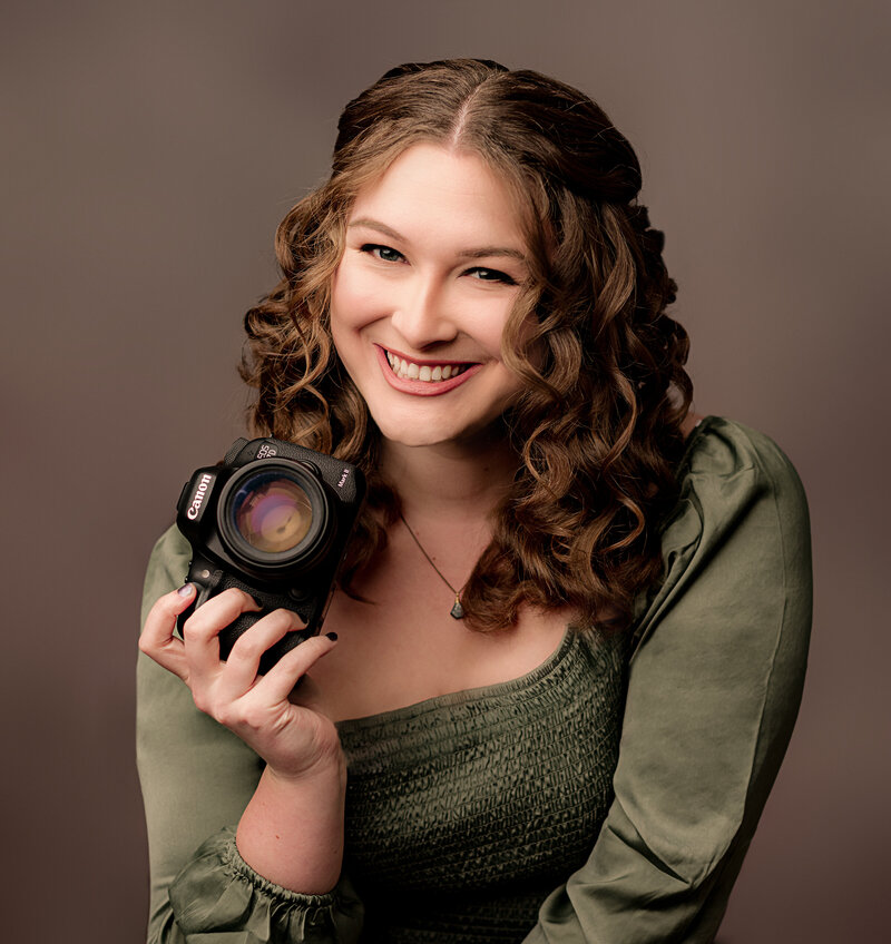 Newborn photographer poses for headshot sitting on stool smiling at the camera