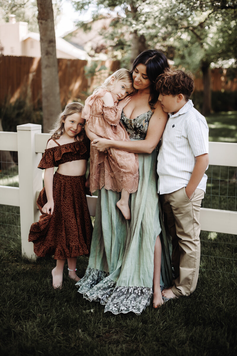 A mother stands with her three young kids in front of a picturesque white picket fence at the Urban Farmhouse in Boise Idaho. 