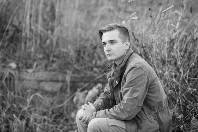 perry high school senior guy sitting among tall grass, photo is black and white, senior is looking away from camera, photographed by Jamie Lynette Photography canton ohio senior photographer