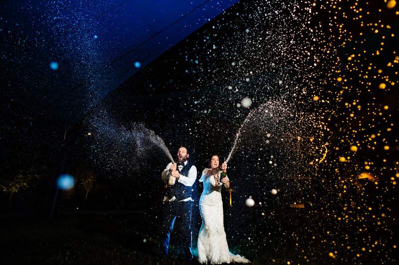 A wedding couple popping champagne at night after the wedding.