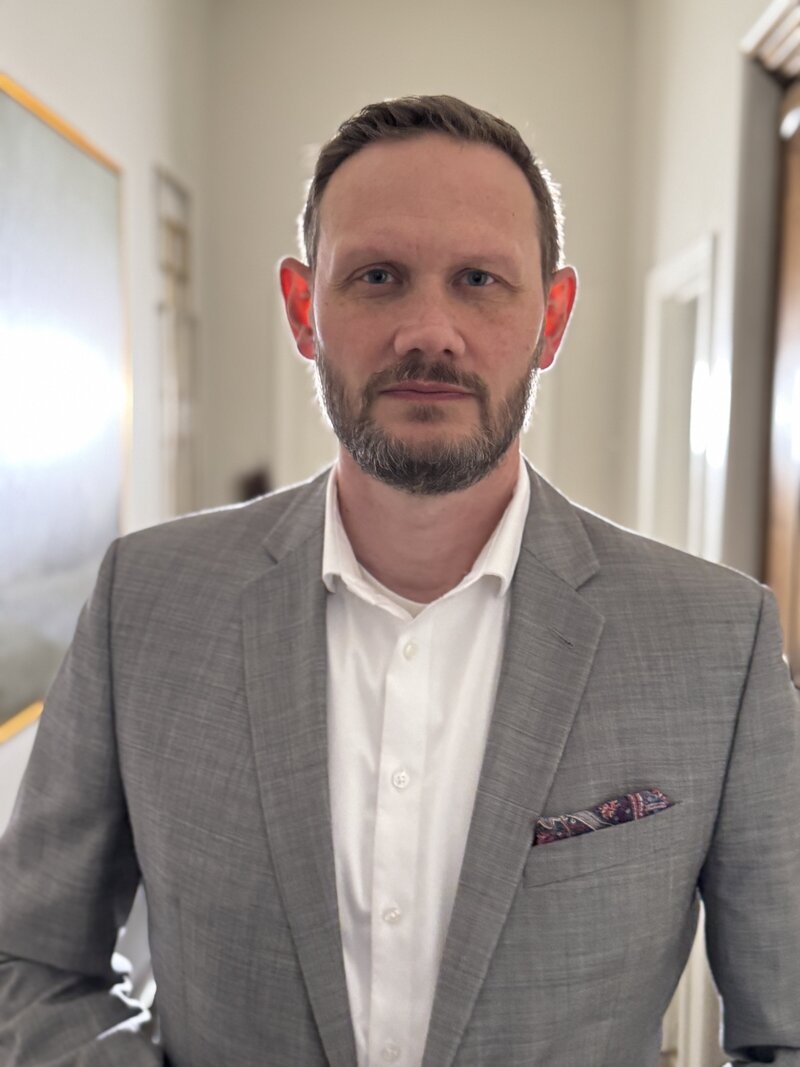 middle-aged man in suit with pocket square and no tie, serious and professional expression with a profound look in his eyes