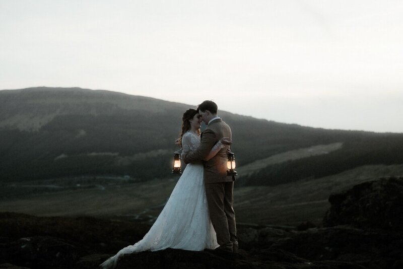 Couple stand in between two mountains and hold each other during sunset in Glencoe, Scotland